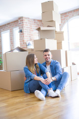 Young beautiful couple in love moving to new home, sitting on the floor very happy and cheerful for new apartment around cardboard boxes