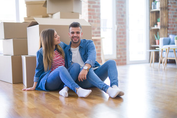Fototapeta na wymiar Young beautiful couple in love moving to new home, sitting on the floor very happy and cheerful for new apartment around cardboard boxes