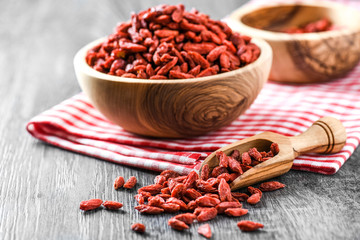 Goji in wooden bowls with green leaves. Goji in scoop. Pile of goji on table.