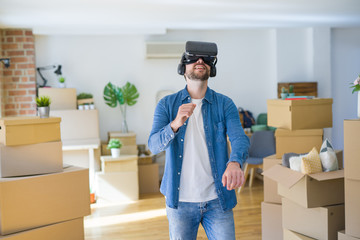 Obraz na płótnie Canvas Young man wearing virtual reality glasses playing a simulation game around cardboard boxes moving to a new house