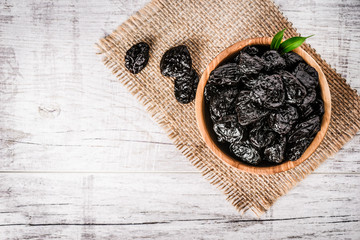 Prunes in wooden bowl on old rustic table. dried plums on table. Top view of prunes on old white board.