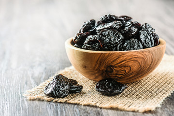 Prunes in wooden bowl on table. Pile of fresh tasty prunes. Dried plums.