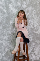 Beautiful child teenager girl sends a kiss. Girl sitting on a chair against a gray wall