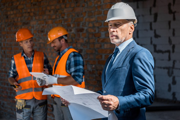 selective focus of businessman holding blueprint near constructors
