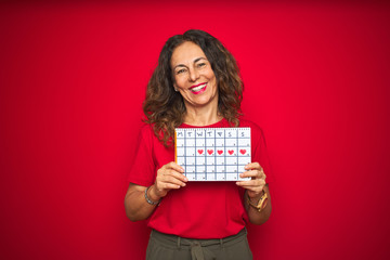 Middle age senior woman holding menstruation calendar over red isolated background with a happy face standing and smiling with a confident smile showing teeth