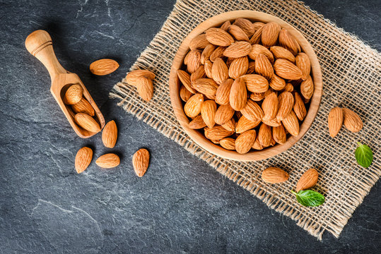 Top view of almonds on dark stone talbe with wooden spoon or scoop. Almonds in wooden bowl. Almonds laid freely on dark table. - Powered by Adobe