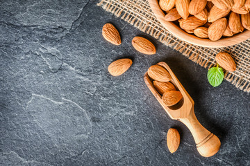 Top view of almonds on dark stone talbe with wooden spoon or scoop. Almonds in wooden bowl. Almonds laid freely on dark table.