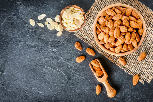 Top view of almonds on dark stone talbe with wooden spoon or scoop. Almonds in wooden bowl. Almonds laid freely on dark table.