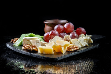 Plate with cheeses, grapes, walnuts. Laid out on black slate.