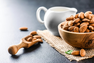 Almonds on dark stone table. Fresh peeled almonds in bowl. Almonds in scoop and milk in ceramic jar.