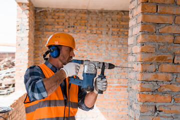 handsome bearded man using hammer drill near brick wall