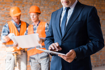 cropped view of businessman holding digital tablet near constructors