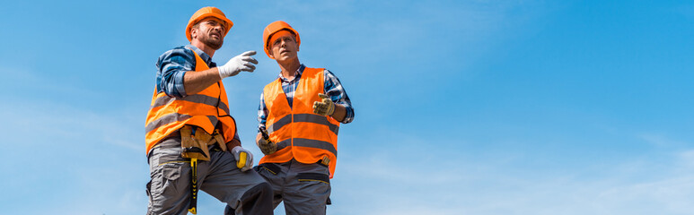 panoramic shot of coworkers in orange helmets standing on rocks against sky