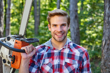 Strong lumberjack with chainsaw in a plaid shirt. Lumberjack worker walking in the forest with...