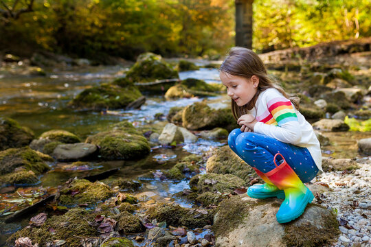 Outdoor recreation and awesome adventures with kids. A little child girl is walking along a green river in the forest in rubber boots on a warm autumn day.  exploring nature, travel, family vacation.