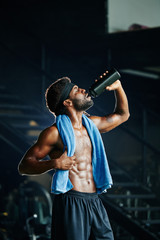 Handsome fit Black man with towel drinking fresh vitamin water after working out hard in the gym