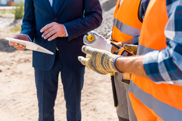 cropped view of constructor holding walkie talkie near coworker and businessman with digital tablet