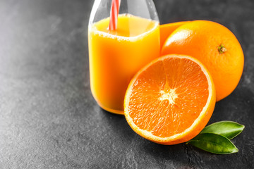 Orange nectar in glass bottle with red straw. Oranges on dark stone table. Fresh oranges and juice in flask.