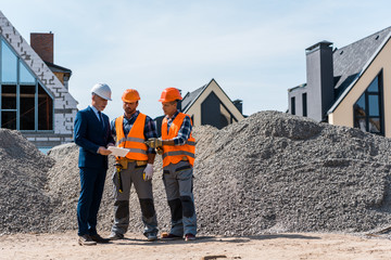 constructors standing near businessman with digital tablet
