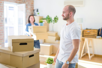 Fototapeta na wymiar Young couple arround cardboard boxes moving to a new house, bald man standing at home looking to side, relax profile pose with natural face with confident smile.