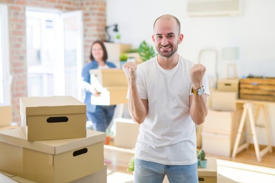 Young couple arround cardboard boxes moving to a new house, bald man standing at home celebrating surprised and amazed for success with arms raised and open eyes. Winner concept.