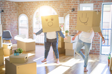 Crazy couple wearing cardboard boxes with funny emoji faces over head, having fun at new house