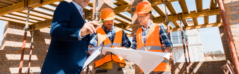 panoramic shot of businessman near builders holding blueprint