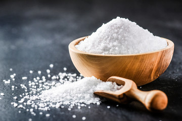 Salt in wooden scoop on dark stone table.