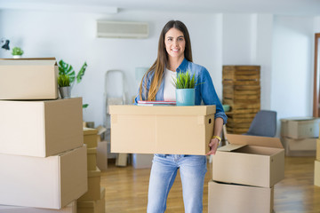 Beautiful young woman holding cardboard box at new apartment, smiling very happy moving to a new house