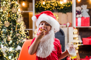 Kid Santa Claus enjoying in served gingerbread cake and milk. Greeting Christmas card.