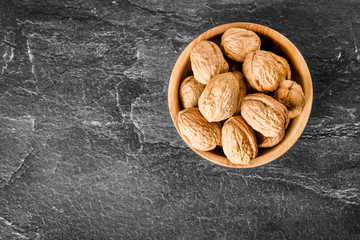 Walnuts top view. Walnut in bowl on black background. Whole walnuts on dark stone table.
