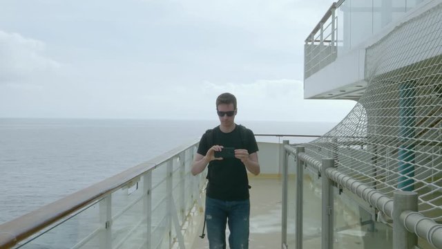 A young man is taking a video of a german luxury cruiseship with a smartphone.