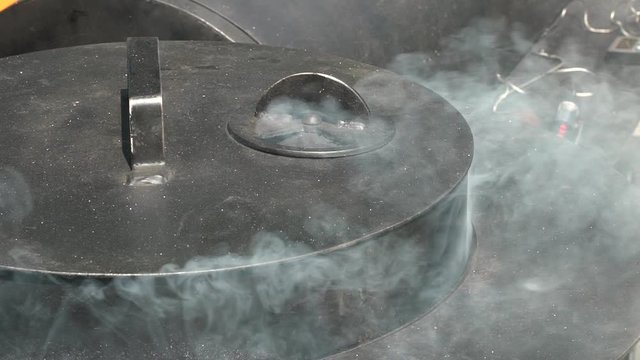 Smoke rise from grill pot lid. Handheld shot