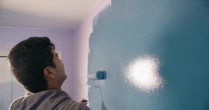 Asian teenager painting bedroom wall blue with paint roller in 4K slow motion