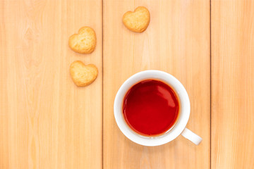 Cup of tea and sweet cookies in shape of heart on wooden background.