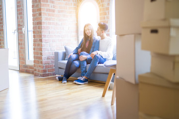 Beautiful young asian couple relaxing together sitting on the sofa arround cardboard boxes, happy moving to a new house