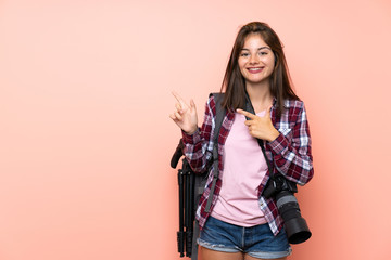 Young photographer girl over isolated pink background pointing finger to the side