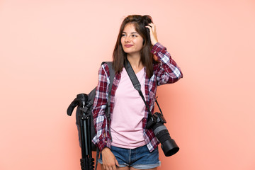 Young photographer girl over isolated pink background having doubts and with confuse face expression