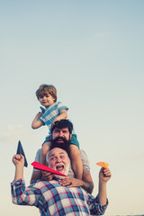 Men generation. Kids playing with simple paper planes on sunny day. Father giving son ride on back...