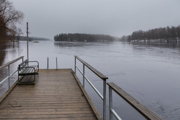 Small pier at beach on Lake Ruotsalainen at cloudy, winter day, Finland.