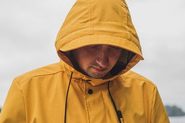 Young man wearing yellow raincoat standing at a lake.