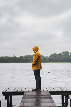 Young man wearing yellow raincoat standing at a lake.