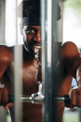 Smiling fit Black man doing exercises with pulldown machine in gym