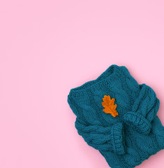 Flat lay top view turquoise cozy knit sweater with oak dry leaf on pink background