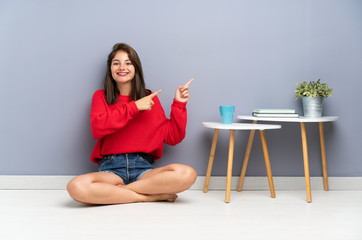 Young woman sitting on the floor pointing finger to the side