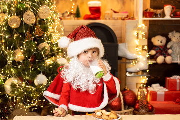 Fototapeta na wymiar Santa Claus eating cookies and drinking milk on Christmas Eve. Little Santa picking cookie and glass of milk at home. Merry Christmas and happy new year.
