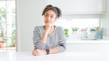 Beautiful african american woman with afro hair wearing casual striped sweater with hand on chin thinking about question, pensive expression. Smiling with thoughtful face. Doubt concept.