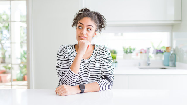 Beautiful african american woman with afro hair wearing casual striped sweater with hand on chin thinking about question, pensive expression. Smiling with thoughtful face. Doubt concept.