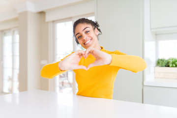 Beautiful african american woman with afro hair wearing a casual yellow sweater smiling in love doing heart symbol shape with hands. Romantic concept.