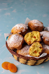 Homemade muffins with dried apricots sprinkled with powdered sugar on a light blue background, vertical orientation, closeup, copy space